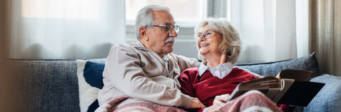 Two seniors enjoying a book together on the couch